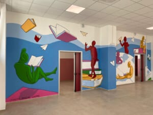 Atrio scolastico decorato con murale di lettori e libri volanti