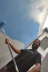 L'artista mentre dipinge il cielo di un murale con un rullo