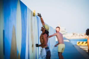 Artisti che dipingono il muro azzurro del molo