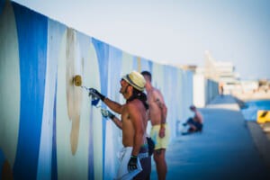 Artista con cappello mentre dipinge il murale del molo