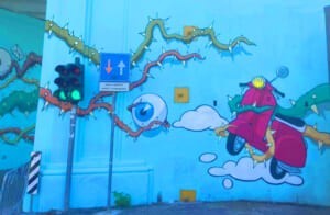 Murale "The World of Camillas" con uno scooter rosso e un semaforo