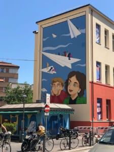 Murale sulla facciata di un edificio con aeroplanini di carta e bambini