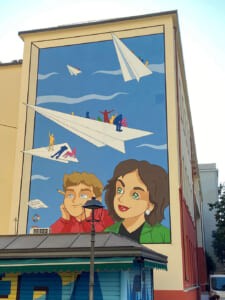 Murale sulla facciata esterna di un edificio con bambini e aeroplanini di carta